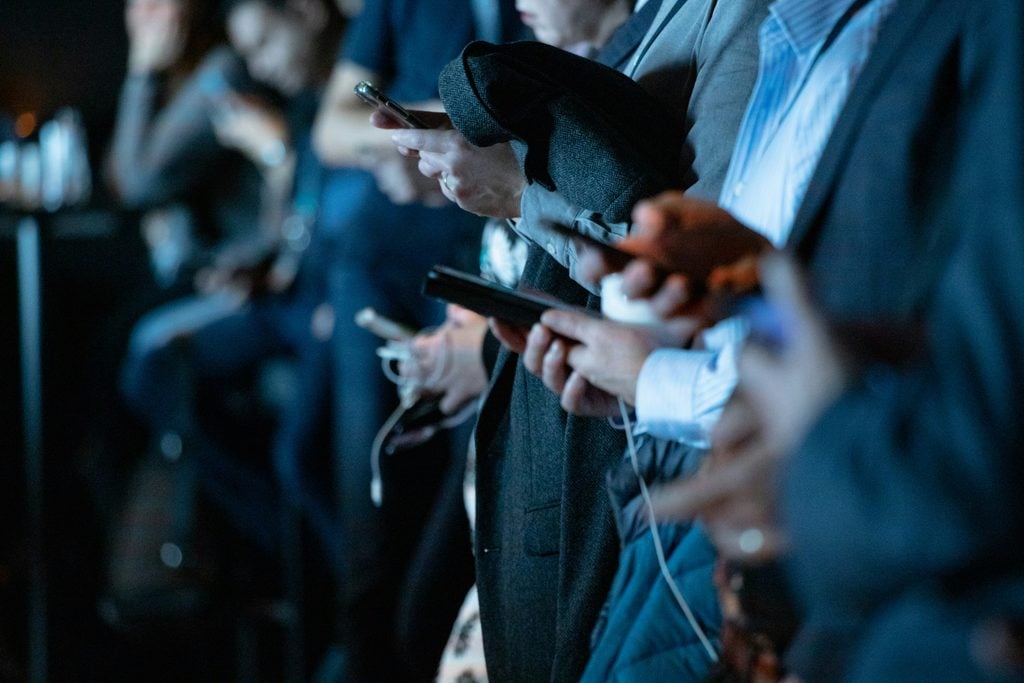 a group of professionals on their phones to illustrate the question "does working from home increase your distraction from social media more than working from an office?"