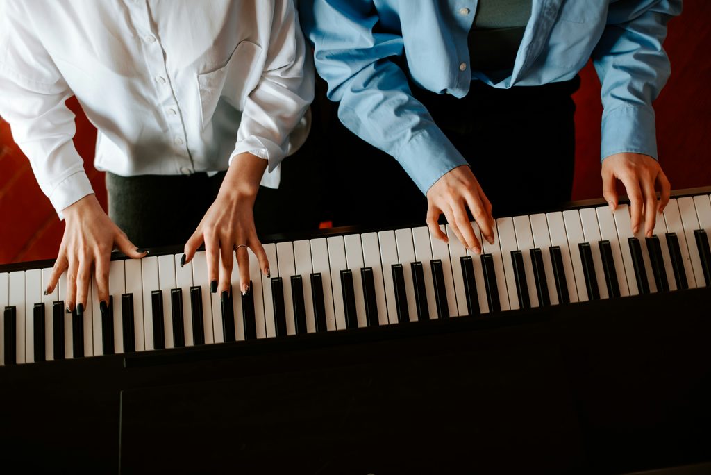 image of two people playing piano to represent a piano lesson featured in our music school story
