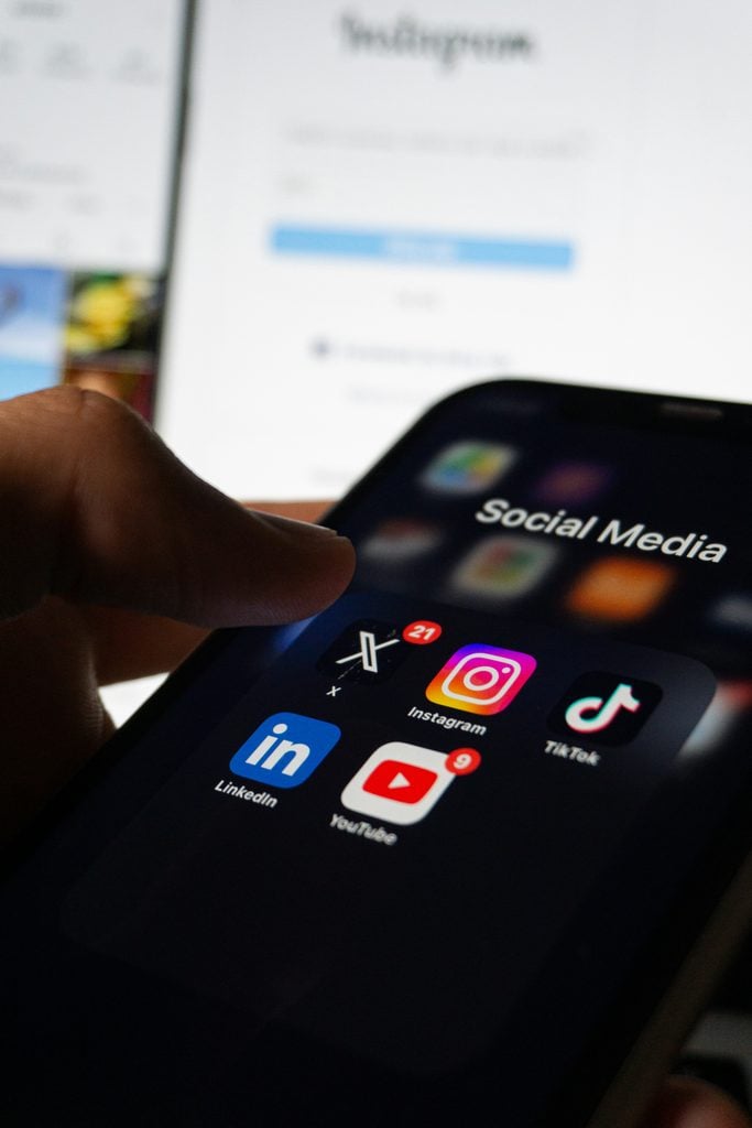 person with a phone open to their social media apps showing logos of major sites used to illustrate focusing first social second workflow